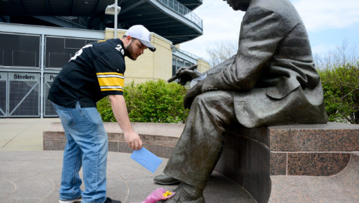 Robert Turner, 31, of Fox Chapel places a card at the Art Rooney statue outside Heinz Field. (Lake Fong/Post-Gazette)