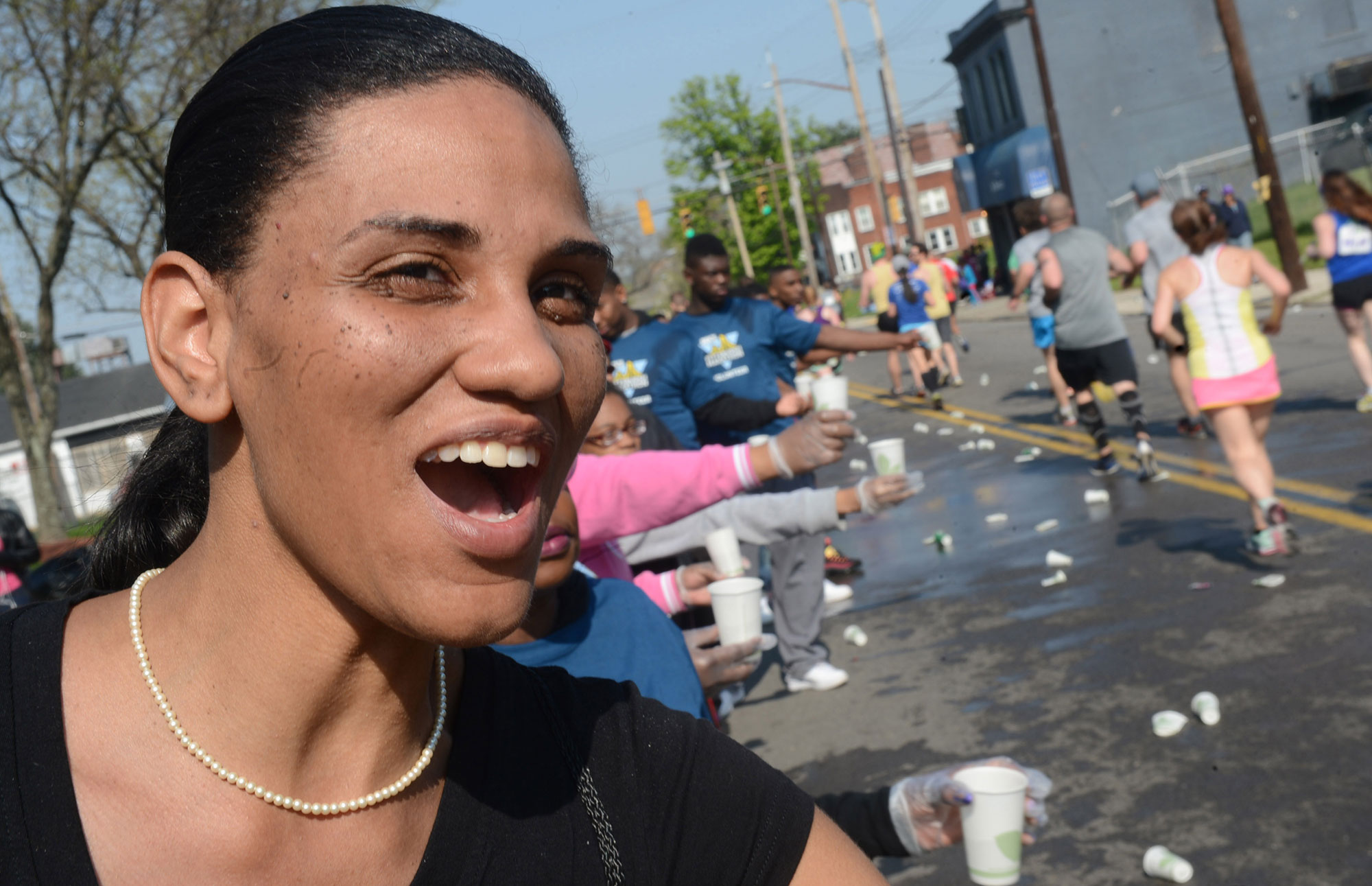 Volunteer Erica Motley cheers and hands water to runners as they make their way down Frankstown Avenue in Homewood. (Nate Guidry/Post-Gazette)