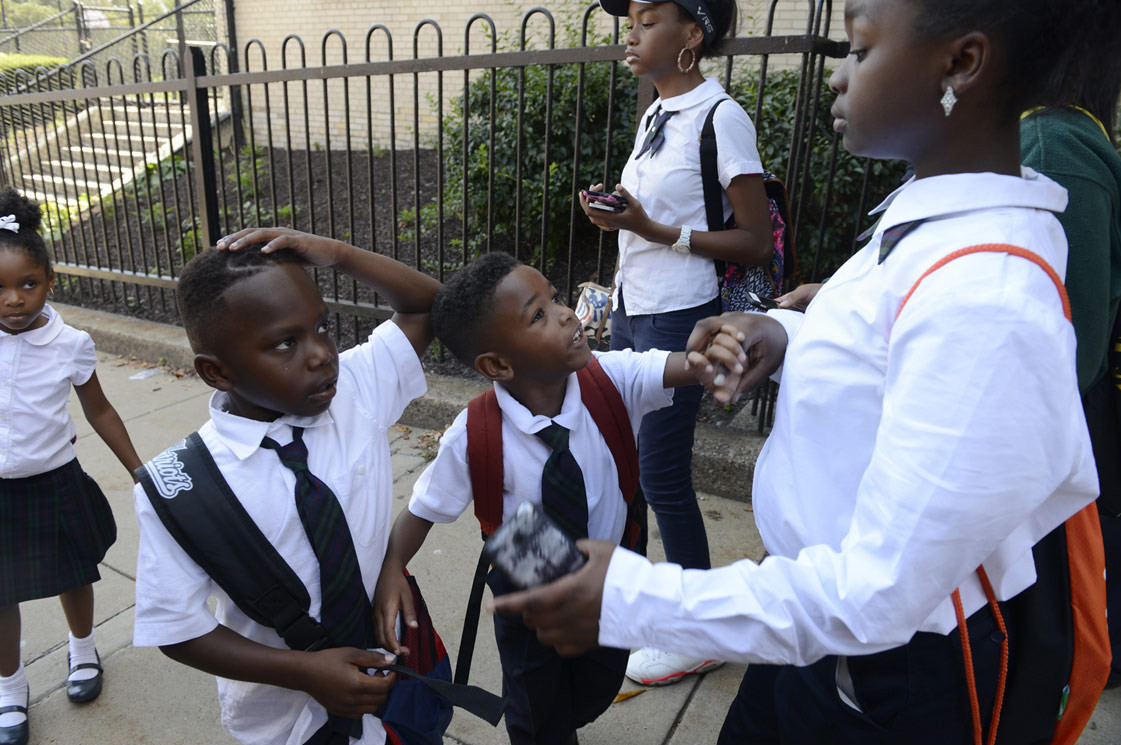 Landon Claybourne, left, 6, and Amoni Thompson, 6, center, wait to board the school along with Jazmine Hale, 13, at St. Benedict the Moor in the Hill District on Aug. 24, 2015. Jazmine escorted kindergarteners to the bus to make sure they knew which one to get on. (Rebecca Droke/Post-Gazette)